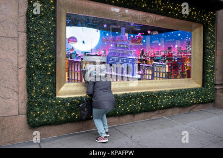 Eine Frau durch ein Vergrößerungsglas für eine Nahaufnahme von Macy's Weihnachten Fenster am Herald Square in Manhattan, New York City suchen. Stockfoto