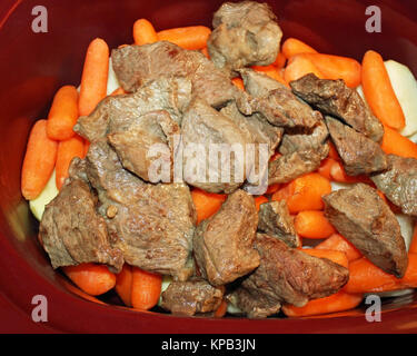 Schichten von in Scheiben geschnittenen Kartoffeln, geschält mini Karotten und goldbraun schmoren Rindfleisch in einer Slow Cooker Stockfoto