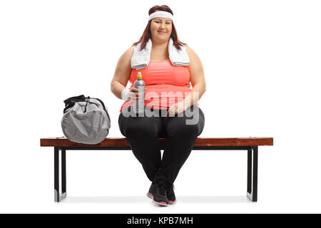 Übergewichtige Frau mit einem Handtuch und eine Flasche auf einer Bank sitzen auf weißem Hintergrund Stockfoto