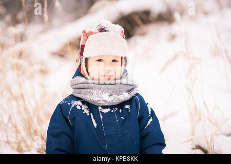 Portrait von niedlichen kleinen lustig Kind in blauer Winter thermische obere Kleidung spielen mit Schnee. Aktiv im Freien Freizeit der Kinder. Stockfoto