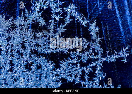 Eiskristalle am Fenster gegen einen kalten, blauen Hintergrund Stockfoto