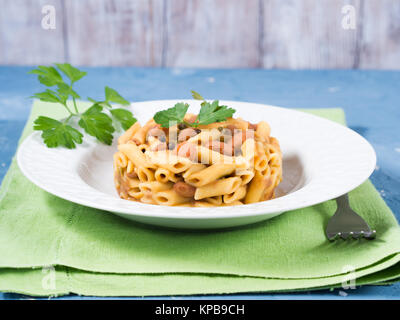 Serviert traditionelle italienische Penne Pasta mit Bohnen auf weiße Platte und blauem Hintergrund Stockfoto