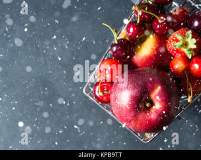 Frisches Obst und Beeren, Kirschen, Pfirsiche und Erdbeeren - in einem Supermarkt Warenkorb auf schwarzem Hintergrund. Kopieren Sie Platz. Nahaufnahme. Ansicht von oben. Fallenden Schnee Stockfoto