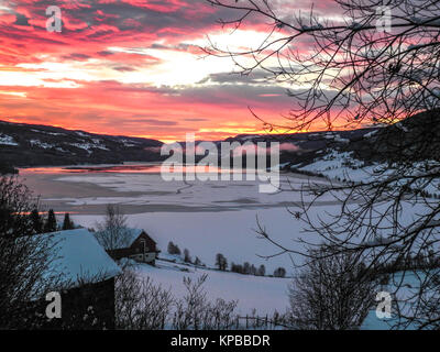 Ein dramatischer Sonnenaufgang hinter den Bergen auf einem vereisten See. Stockfoto