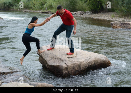 Mann, Frau, auf die großen Felsen in der Mitte der Fluss springen, aber halten ihre Hände bei Clear Creek White Water Park Stockfoto