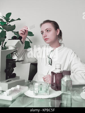 Junge weibliche microscopist im weißen Mantel wählt eine Gewebeprobe für mikroskopische Analyse Stockfoto