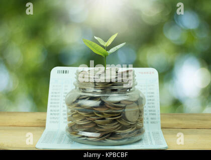 Sparen und Geld Konzept, gestapelte Münzen mit Bäumchen wachsen oben auf Gläser und buchen Sie Banken auf Holz Tisch und Grünen bokeh Hintergrund Stockfoto