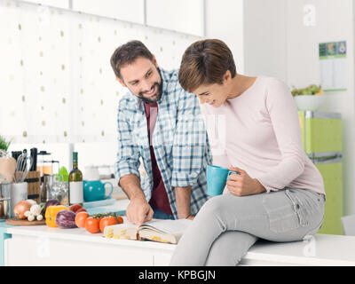 Glückliches junges Paar in der Küche suche Rezepte im Kochbuch, Beziehungen und Lifestyle Konzept Stockfoto