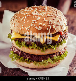 Lecker double Cheeseburger mit einer Platte des geschmolzenen Käse über zwei rindfleischpastetchen auf einem knackigen Salat auf einem sesambrötchen, Nahaufnahme, Seite, Ansicht auf einem rustikalen Holzmöbeln Zähler Stockfoto