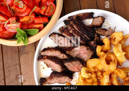 Flanke Steak mit Pommes frites in Ringe geschnittenen Zwiebeln und Salat Stockfoto