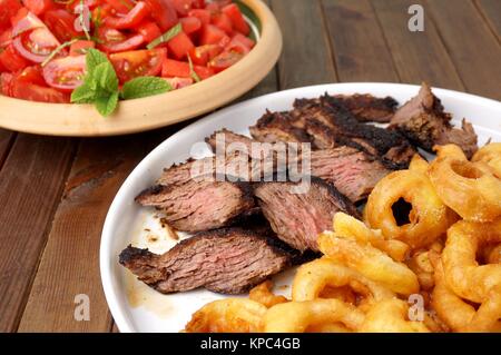 Flanke Steak mit Pommes frites in Ringe geschnittenen Zwiebeln und Salat Stockfoto