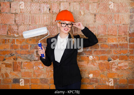 Porträt des Architekten student oder Maler mit farbroller und Schutz Helm tragen. Ziegelrot Hintergrund. Stockfoto