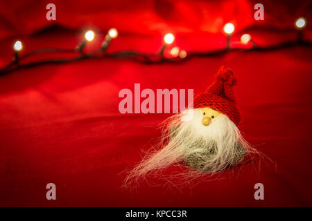 Nahaufnahme der niedliche Weihnachtsmann Puppe mit langen, weißen Bart, Weihnachten Dekoration isoliert. Roter Stoff Hintergrund und verschwommen Lichter Stockfoto