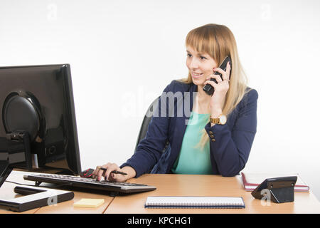 Die Frau, die in der Computer- und sprechen über das Telefon Stockfoto