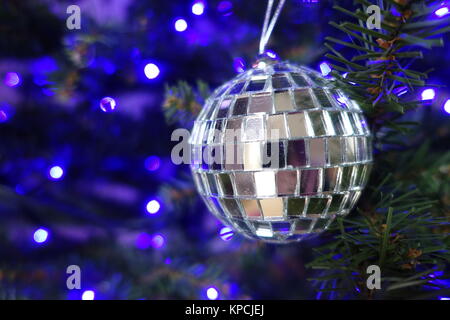 Silberne Kugel hängt an einem Weihnachtsbaum mit blauen Lichtern im Hintergrund Stockfoto