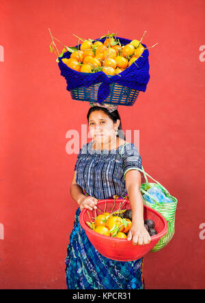 ANTIGUA, GUATEMALA - Dec 23, 2015; Unbekannte junge GUATEMALTEKISCHE Frau trägt Früchte in einer Körbe auf dem Kopf, die Hände am 23.Dezember 2015, Antigua, Guatemala Stockfoto