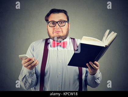 Chubby Kerl in der Brille die Wahl zwischen Buch und Smartphone lesen. Stockfoto