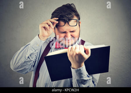Mollig Mann halb geschlossenen Augen und haben Probleme mit dem Lesen Buch. Stockfoto