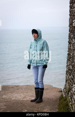 Angst und Kälte suchen Mädchen in Gummistiefel, Jacke, Handschuhe und Kapuze gekleidet, auf der der Kante, die durch das Meer, England. Stockfoto