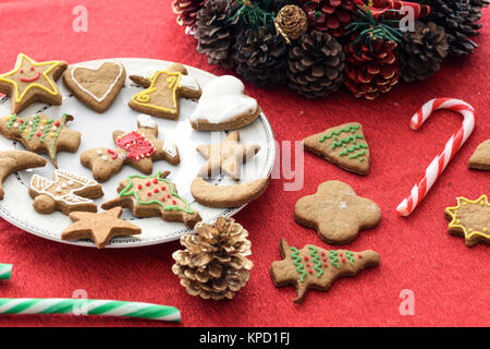 Konzept Bild von Weihnachten Spaß mit Kindern - eine Vielzahl von hausgemachten Lebkuchen auf einer roten Tischdecke mit Dekorationen. Stockfoto