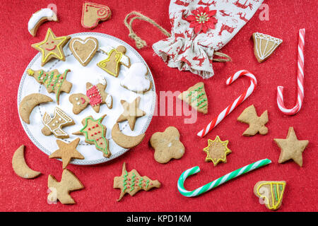 Eine konzeptuelle Bild von Weihnachten Spaß mit Kindern - eine Vielzahl von hausgemachten Lebkuchen auf einer roten Tischdecke mit Dekorationen. Stockfoto