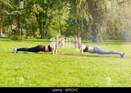 Zwei Frauen dehnen nach dem Sport auf dem Rasen im Park Bäume im Hintergrund Stockfoto