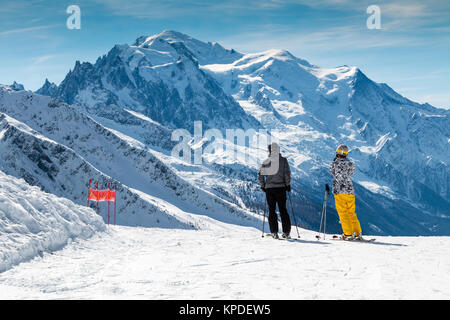 Skifahrer stehend auf eine Skipiste mit Blick über den Mont Blanc im Winter. Die männlichen und weiblichen tragen helle Ski Kleidung. Stockfoto