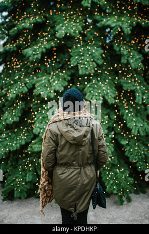 Frau steht vor grossen Weihnachtsbaum Stockfoto