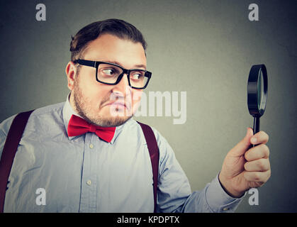 Exzentrische Mann mit Übergewicht in red Bow-tie durch Lupe suchen auf Grau posieren. Stockfoto