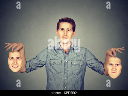 Junger Mann mit Masken Kommissionierung Stimmung für Heute gespaltene Persönlichkeit darstellen. Stockfoto