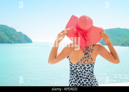 Rückseitige Ansicht des Modells im Stroh Hut auf dem Hintergrund der Lagune von Resort Hotel unter den Bergen posieren. Stockfoto