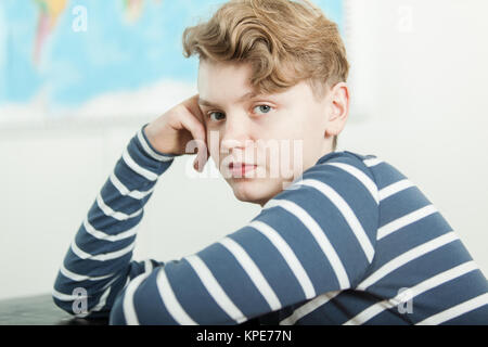 Junge sitzt am Schreibtisch mit dem Kopf auf der Hand Stockfoto