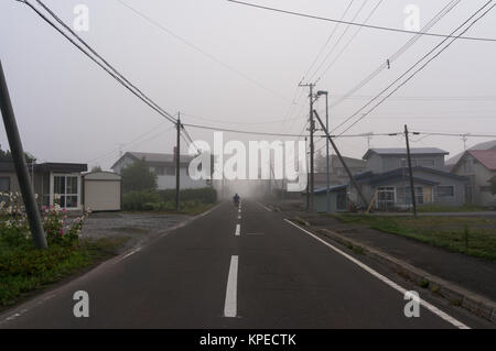 Ein Motorradfahrer, Reiten in der Morgennebel auf dem ruhigen Land japanische Stockfoto