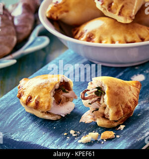 In der Nähe von frisch gekochte Brasilianische empanada zur Hälfte mit Krümel auf Blau Holz Schneidebrett und Schüssel gebrochen Stockfoto