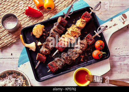 Hohe Betrachtungswinkel und der Vielfalt an gegrillten Fleischspieße durch frische Zutaten und Saucen und serviert auf Pan auf rustikalen Paddel aus Holz umgeben Stockfoto