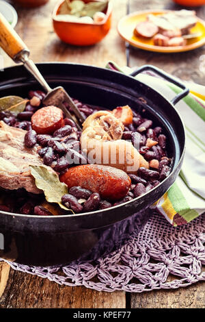 In der Nähe der traditionellen brasilianischen Bohneneintopf mit einer Auswahl an Wurst und Fleisch, serviert in Gusseisen Topf auf Filigrane Deckchen und rustikalen Holztisch Stockfoto