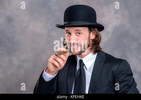 Junge Unternehmer mit Melone im schwarzen Anzug grossen Zigarre rauchen Stockfoto