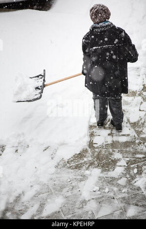 Frau Schaufeln Schnee vom Gehsteig vor seinem Haus nach einem Schneefall in einer Stadt Stockfoto