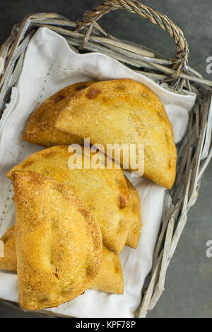 Home gebackene Empanadas Umsatz Torten mit Pisto Gemüse Käse Füllung in Tomatensoße in Weidenkorb auf weißem Leinen Serviette. Spanisch Gebäck. Dunkle Co Stockfoto