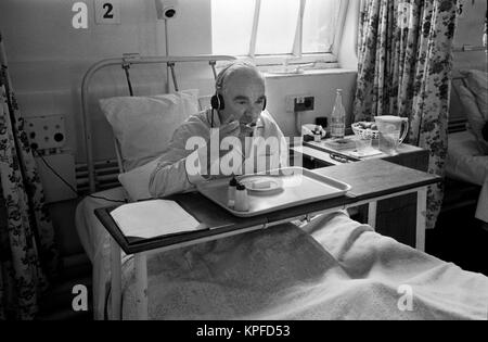 Das 1970er National Health Service (NHS) Charing Cross Hospital. Ein älterer Mann, der im Bett sitzt und sein Mittagessen isst. Er hört Radio und trägt Kopfhörer. Fulham, London, England, ca. 1972. HOMER SYKES Stockfoto