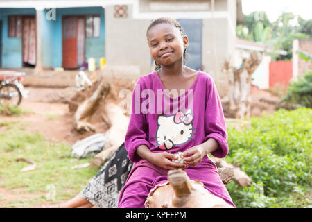 Ein schönes Lachen ugandischen Mädchen sitzen auf einen umgestürzten Baumstamm. Stockfoto