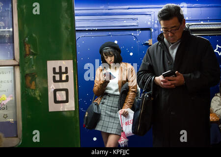 Eine junge Frau und ein Mann, die im Touristeninformationsbüro in einem alten Zugwagen am Hachiko-Platz, Shibuya, Tokio, Japan, Smartphones benutzen. Stockfoto