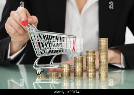 Einkaufswagen mit gestapelten Münzen auf Schreibtisch Stockfoto