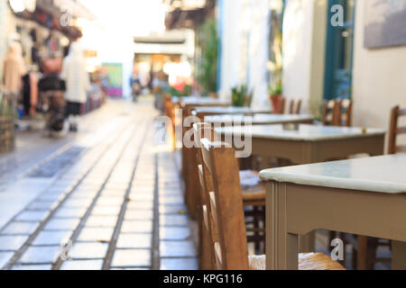 Athen, Griechenland. Griechische Taverne leere Tische und Stühle in einer Reihe, blur Fußgänger- und Markt Hintergrund Stockfoto