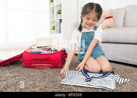 Fröhliche hübsches Kind Kinder Falten Kleidung in Wohnzimmer und Verpackung Gepäck Koffer Vorbereitung Reisen mit der Familie in Urlaub zu gehen. Stockfoto