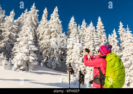 Kaukasische Frau in farbenfrohen Outfit eine Pause von backcountry Skiing ein Bild aufnehmen, Aufnahme der schönen Winterlandschaft Stockfoto