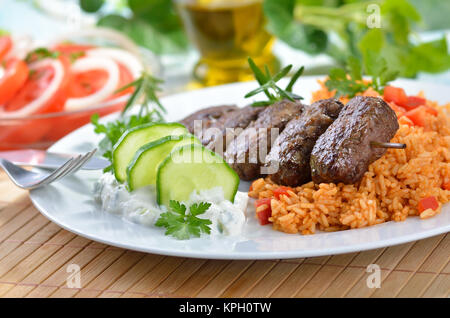 Griechische Frikadellen mit Paprika Reis und tsatsiki, im Hintergrund Tomatensalat mit Zwiebelringen. Stockfoto