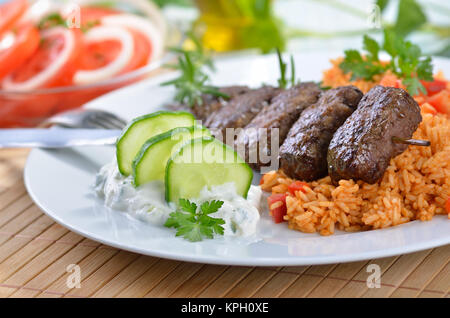 Griechische Frikadellen mit Paprika Reis und tsatsiki, im Hintergrund Tomatensalat mit Zwiebelringen. Stockfoto