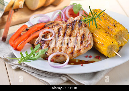 Heiß, lecker, lecker Gegrilltem Schweinefleisch Steak essen mit Mais, Zwiebeln, Paprika und Salat und Brot im Hintergrund Stockfoto