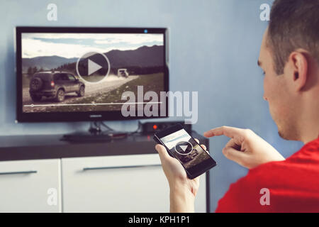 Mann mit Smartphone an einen TV Video zu Hause angeschlossen. Übertragen Sie Videos vom Telefon auf den TV-Bildschirm. Moderne Geräte. Die Informationsübertragung zwischen Dev Stockfoto